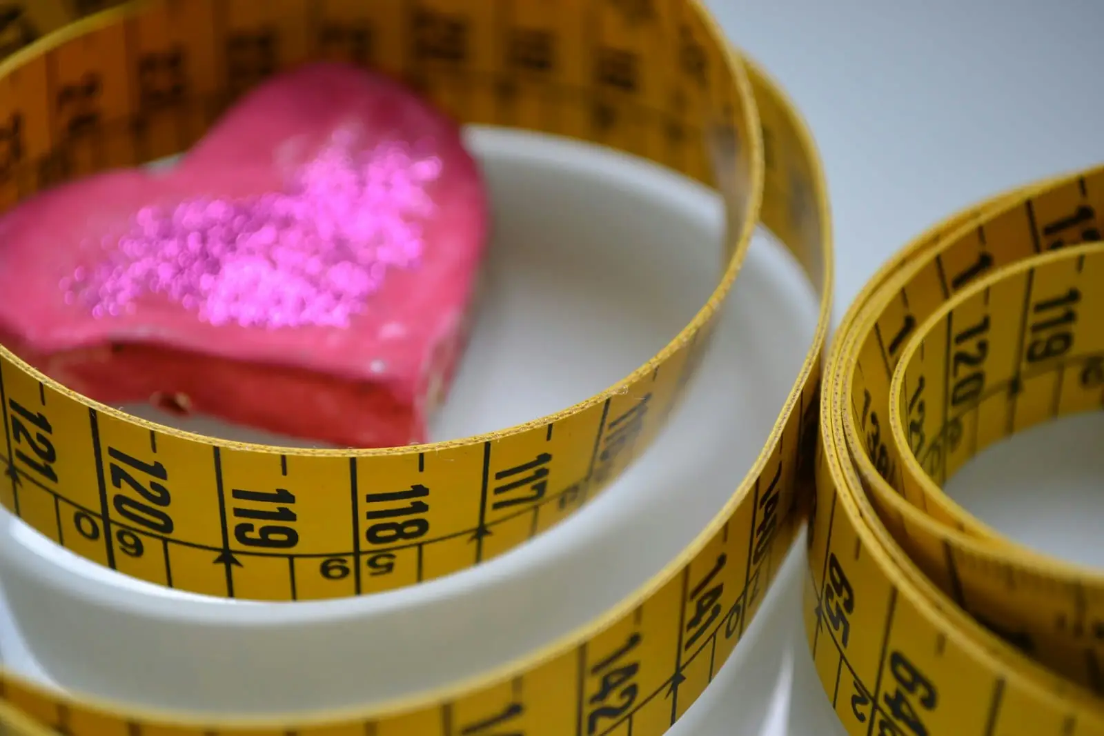A yellow tape measure coiled around a pink heart